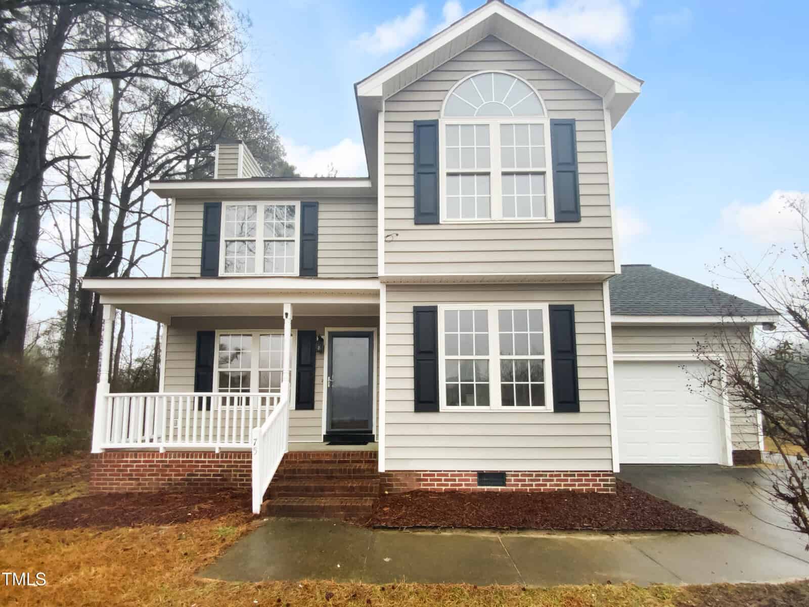 Two-story house with beige siding, dark shutters, a covered front porch, and an attached garage located at 75 Mitchell Store Road in Youngsville. The front yard has a small lawn and a concrete walkway leading to the entrance. Trees are visible beside and behind the house.