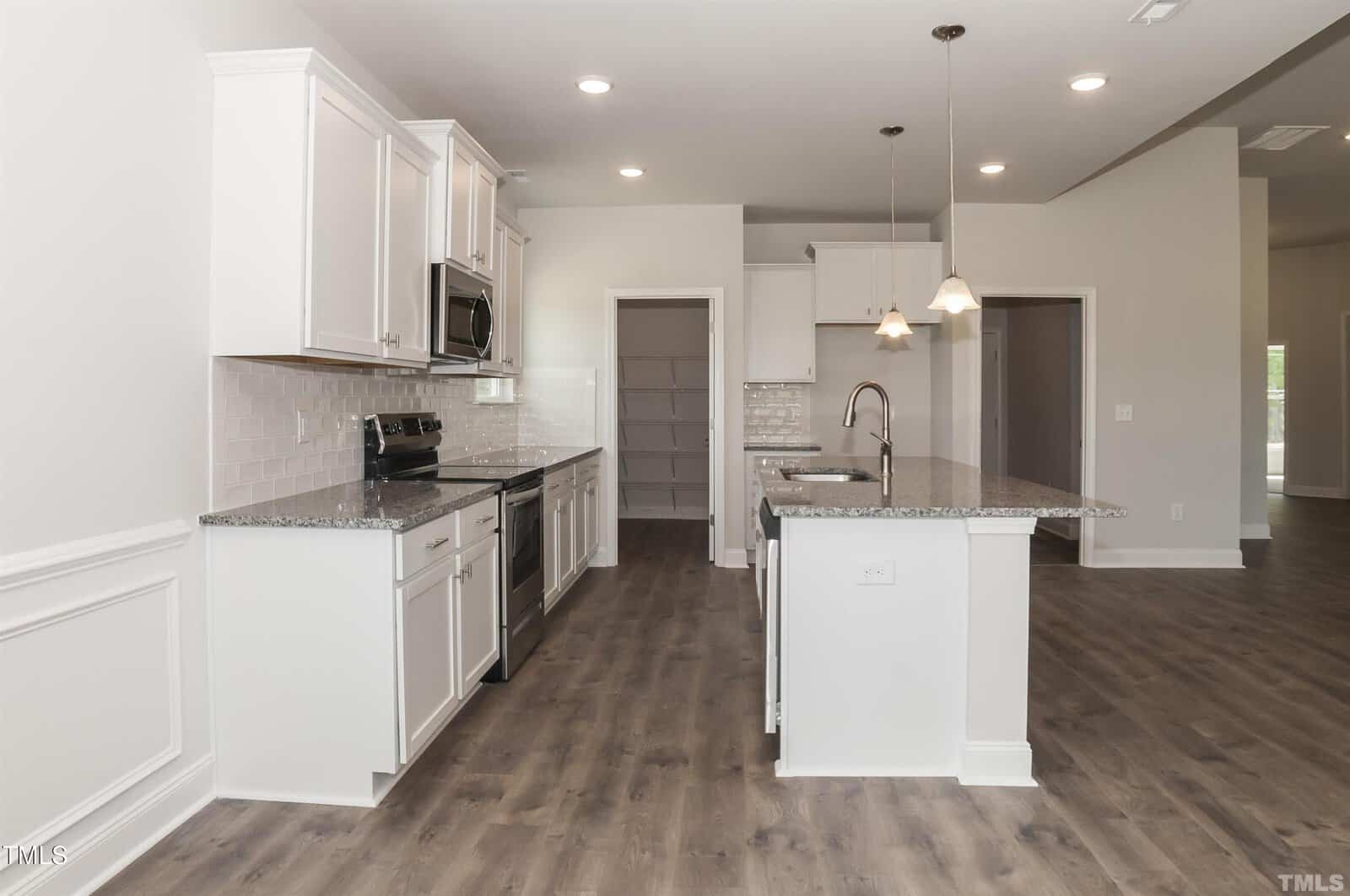Modern kitchen with white cabinets, stainless steel appliances, granite countertops, tile backsplash, pendant lights over a center island, and wood-style flooring. An open doorway leads to a walk-in pantry.