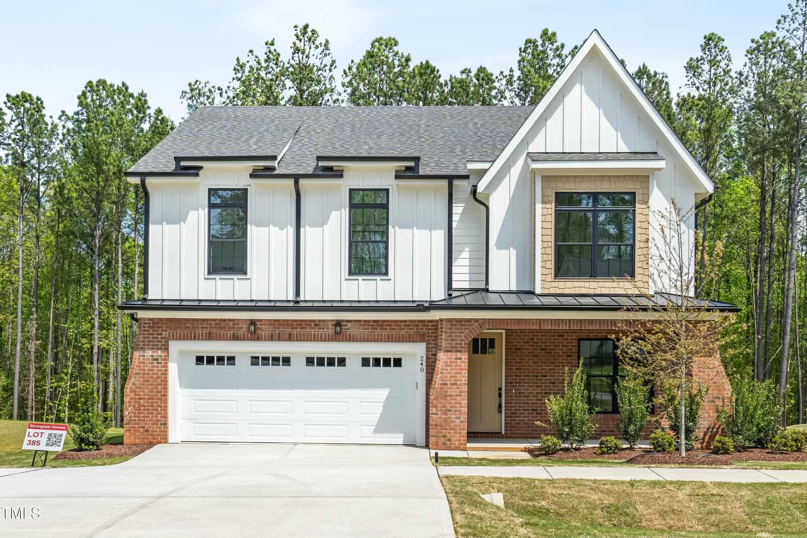 Modern two-story home at 240 Sutherland Drive, Franklinton, with white siding, large black-framed windows, red brick accents, double garage, covered front porch, landscaped yard, and tall pine trees surrounding the property.