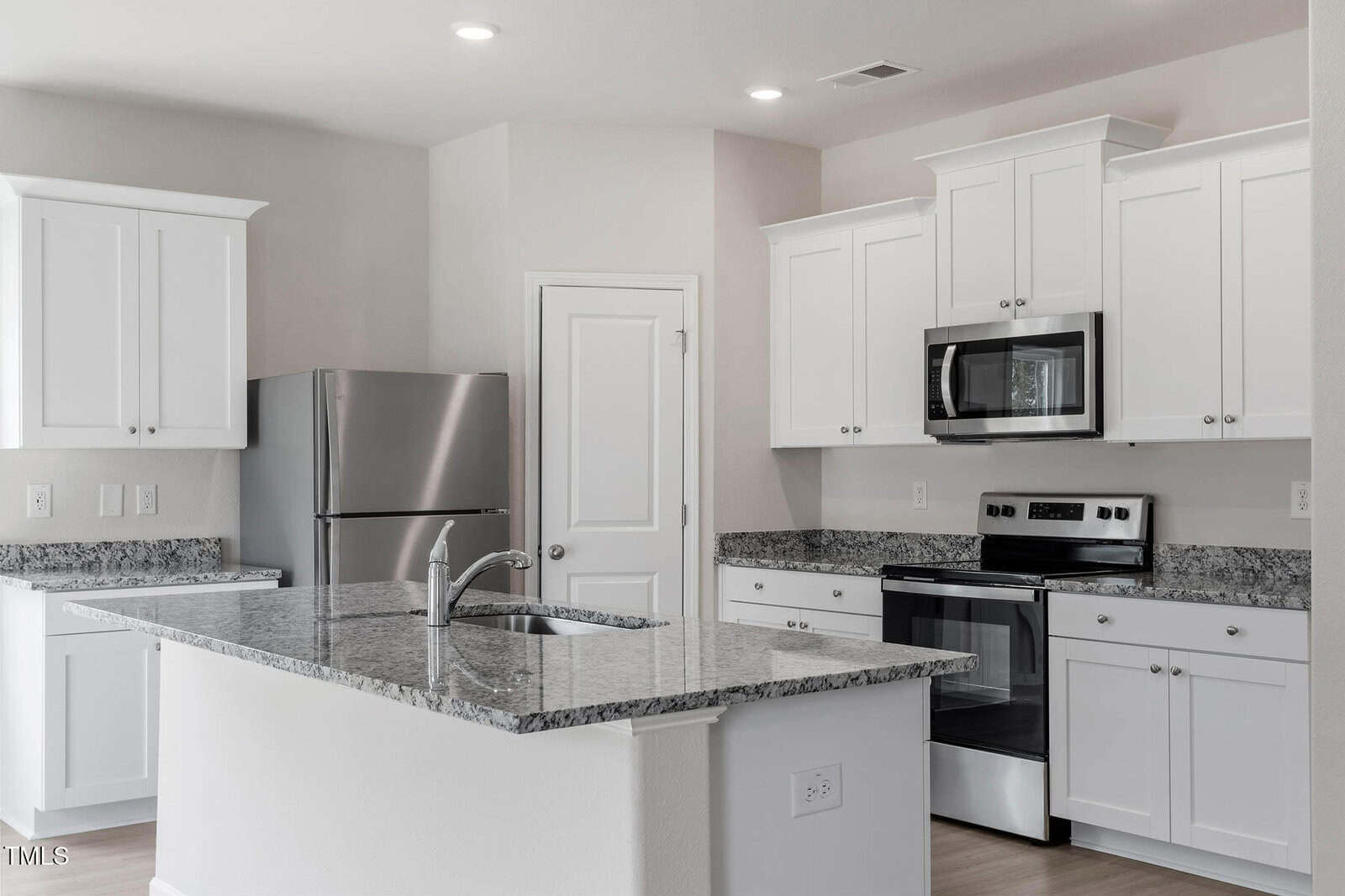 Modern kitchen with white cabinets and a granite countertop. Stainless steel appliances, including a refrigerator, oven, and microwave, are present. The room is well-lit with recessed lighting, and there is a central island with a sink.
