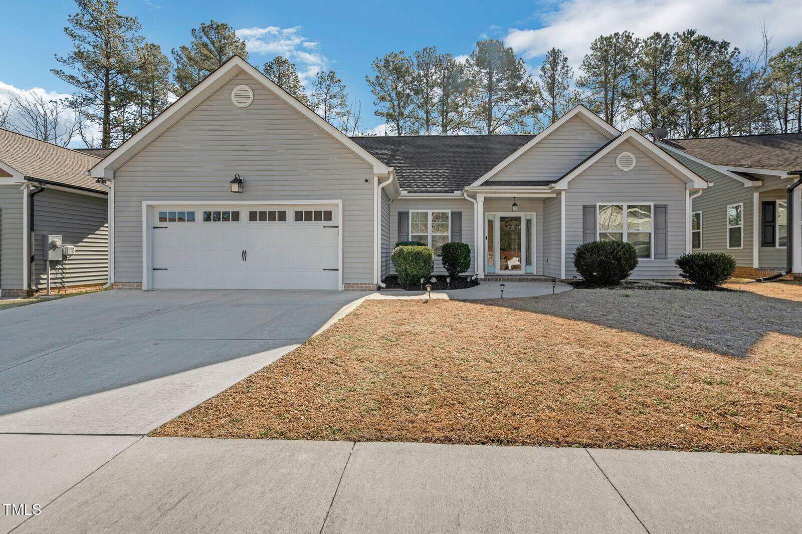 Nestled at 124 Kipling Drive, Oxford, this single-story gray house boasts a two-car garage and a gabled roof. The front yard is adorned with trimmed shrubs and a dry grass lawn, while the concrete driveway and walkway guide you to its entrance. Tall trees rise in the background under a partly cloudy sky.