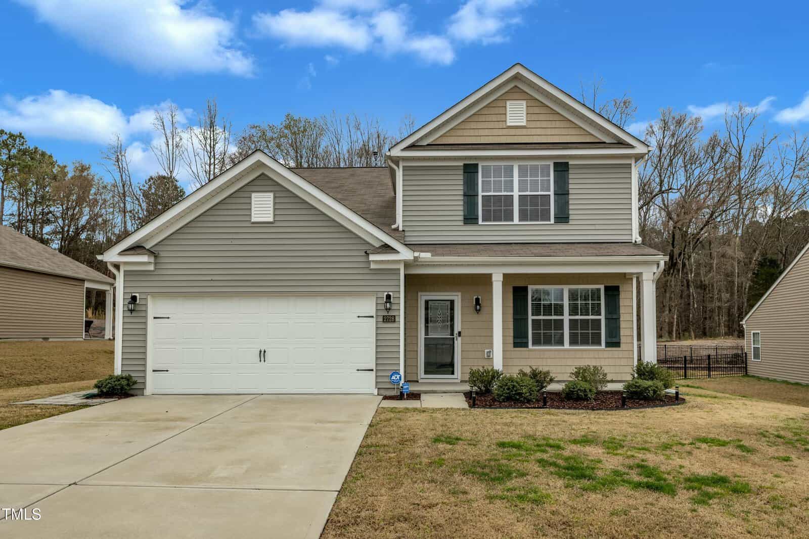 This charming two-story house at 2728 Spring Valley Drive boasts light gray siding with crisp white trim. Set in the heart of Creedmoor, it features a front lawn adorned with bushes, a double garage, and a welcoming brown front door with sidelights on its cozy porch.