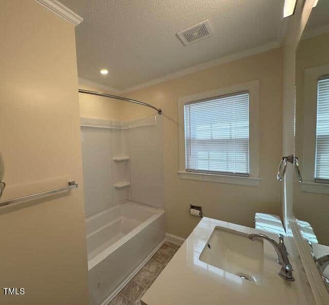 Bathroom with cream-colored walls and a white bathtub with a sliding shower door. The vanity features a sink with a chrome faucet, and a wall-mounted mirror above. Two windows with blinds allow natural light into the room.