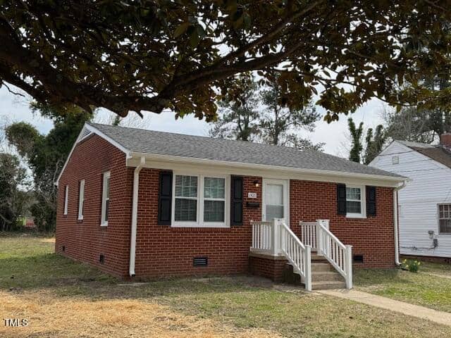 The single-story brick house at 1421 Deer Crossing Court in Henderson features white trim and black shutters. A small set of steps leads to a white front door with a window. The home is enhanced by a quaint front yard with grass and a tree, while another house is partially visible nearby.