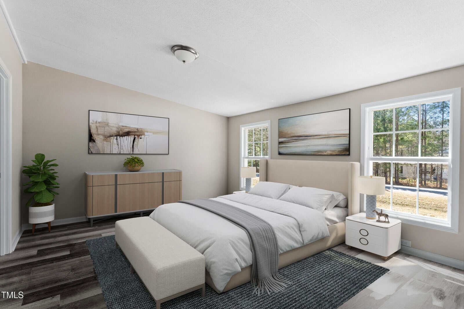 A modern bedroom with a bed, bench, white nightstand, dresser, potted plant, two paintings, large windows letting in natural light, and a view of trees outside. Walls are light-colored, and flooring is wood with a dark rug.