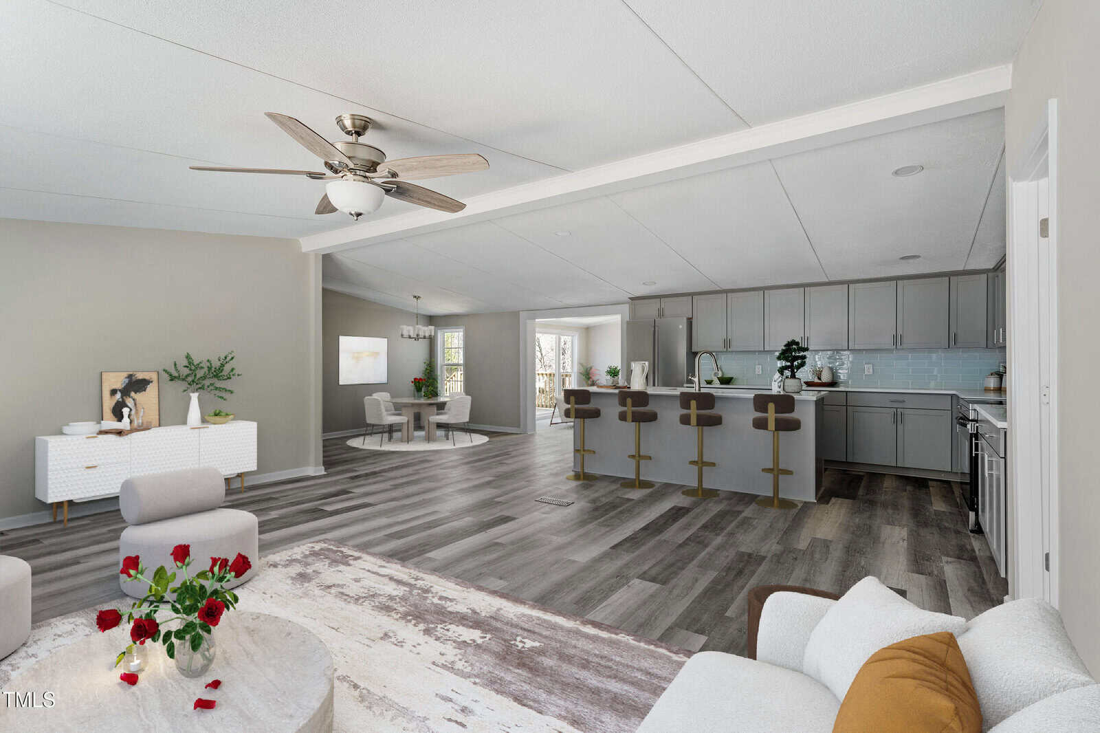Open-concept living space with a modern kitchen featuring gray cabinets, a long breakfast bar with four stools, dining area, and living area with a white armchair, coffee table, and neutral-colored decor.