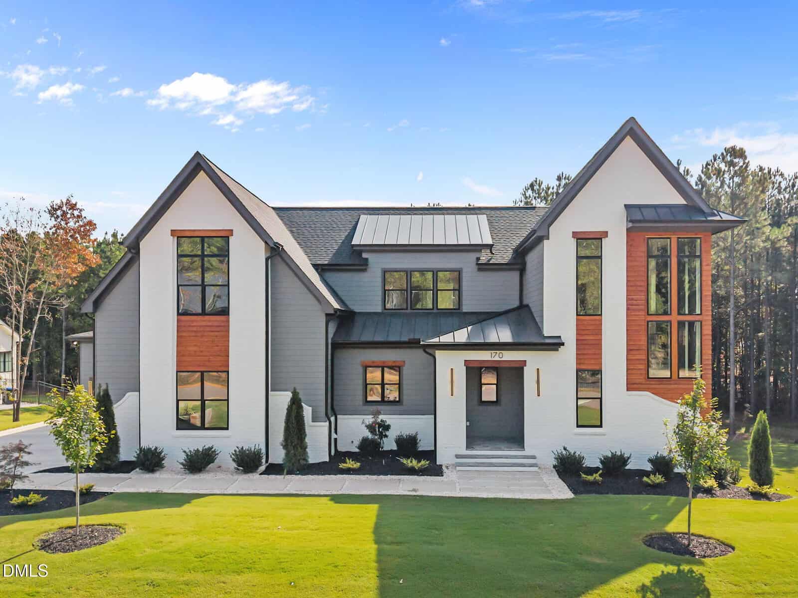 Modern two-story house at 170 Cherry Bark Drive in Youngsville with large windows, gray and white exterior, wood accents, black roof, and a neatly landscaped yard on a sunny day under a blue sky.