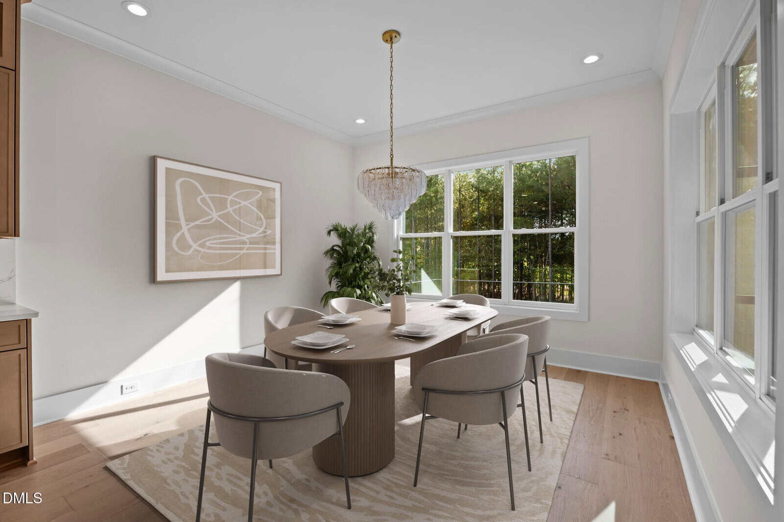 A modern dining room with a round wooden table set for six, beige upholstered chairs, a large abstract artwork on the wall, a chandelier overhead, and large windows letting in natural light.
