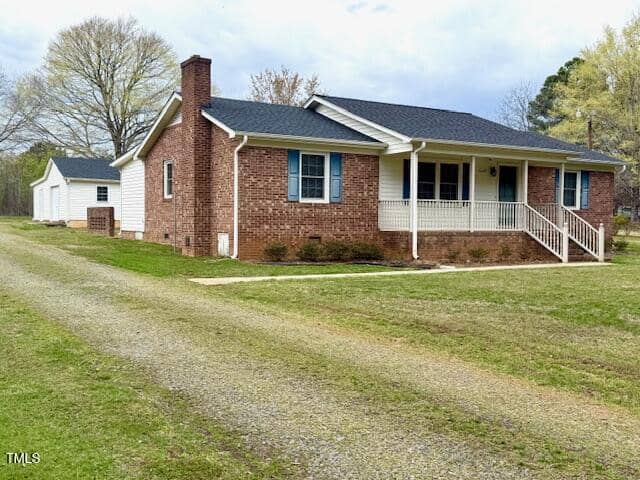 Located at 6527 US 15 in Oxford, this charming single-story brick house features a cozy covered front porch, a side chimney, and a gravel driveway. In the background, you'll find a white outbuilding. The yard is grassy with a few trees adding to its quaint appeal.