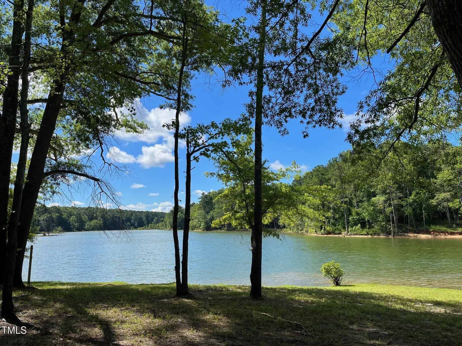 Nestled near Lot 2f Bent Tree Lane, this scenic view of a lake shines under a clear blue sky. The foreground showcases tall trees, while the wooded shoreline in the background enhances its allure. Sunlight dances on the water, creating captivating reflections in this serene Manson haven.