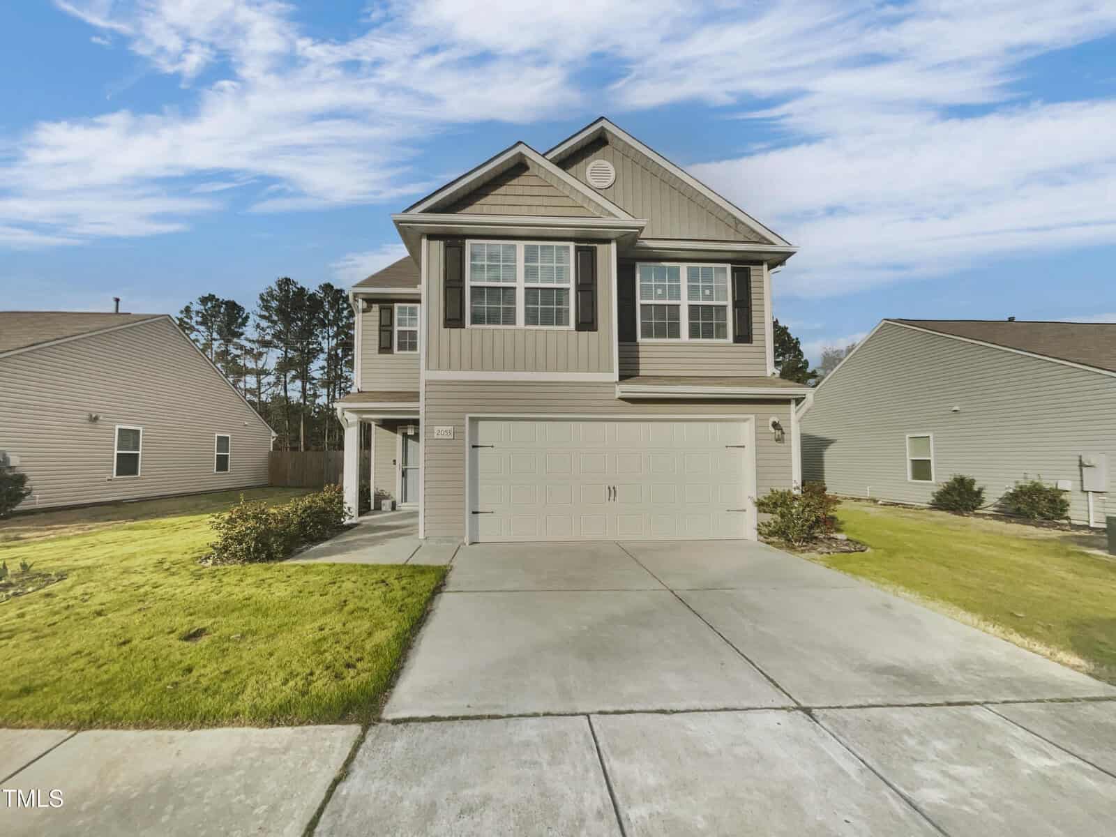 Located at 2053 Alderman Way in Creedmoor, this two-story house features light gray siding and dark shutters. It boasts a two-car garage and a manicured front lawn. The concrete driveway complements the home, which is surrounded by similar houses under a partly cloudy sky.