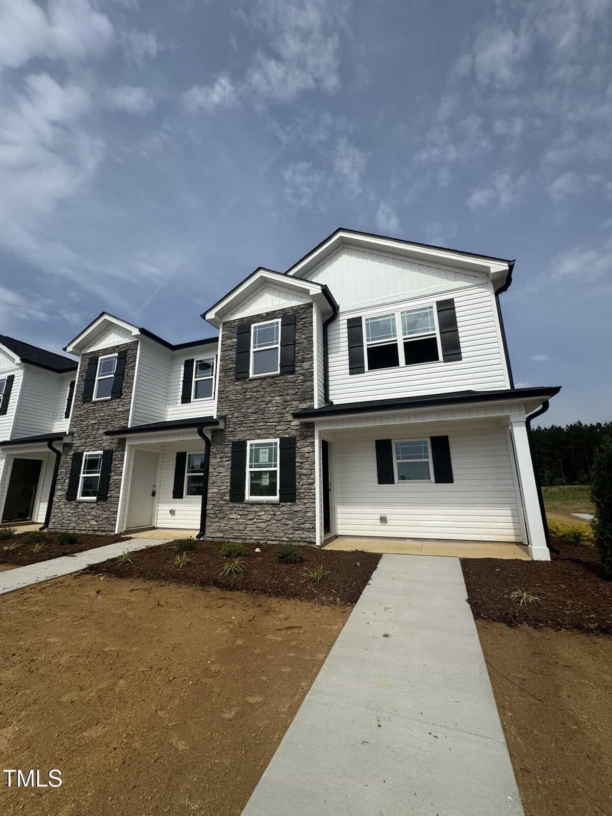 A newly constructed two-story townhouse at 1101 Brookrun Drive, Oxford, features white siding, gray stone accents, multiple windows with black shutters, and a covered entryway. The yard is unfinished with bare ground and a concrete walkway.