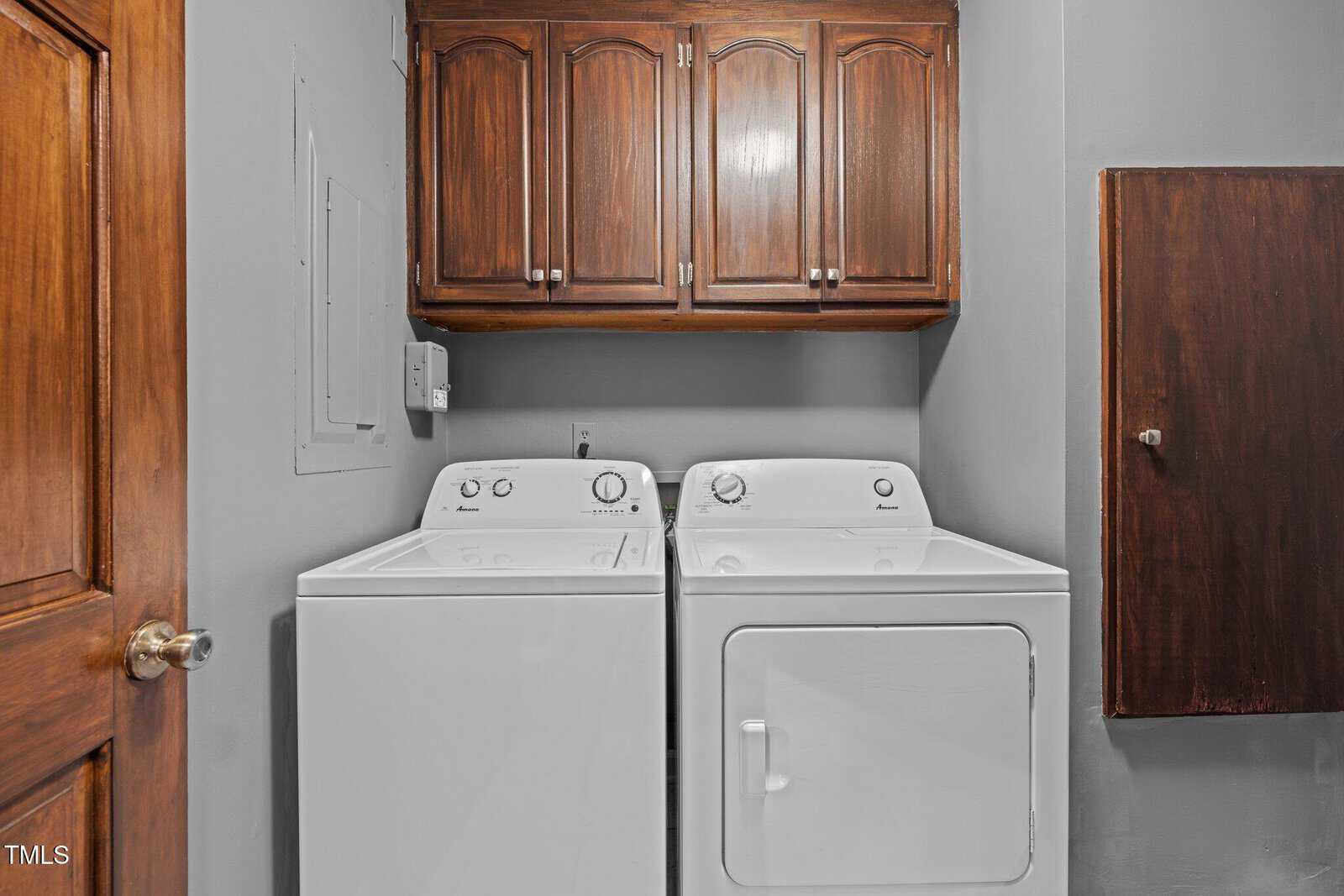 Laundry area featuring a white washing machine and dryer side by side. Above them are wooden cabinets for storage. The walls are painted gray, and there is a wooden door on the left.