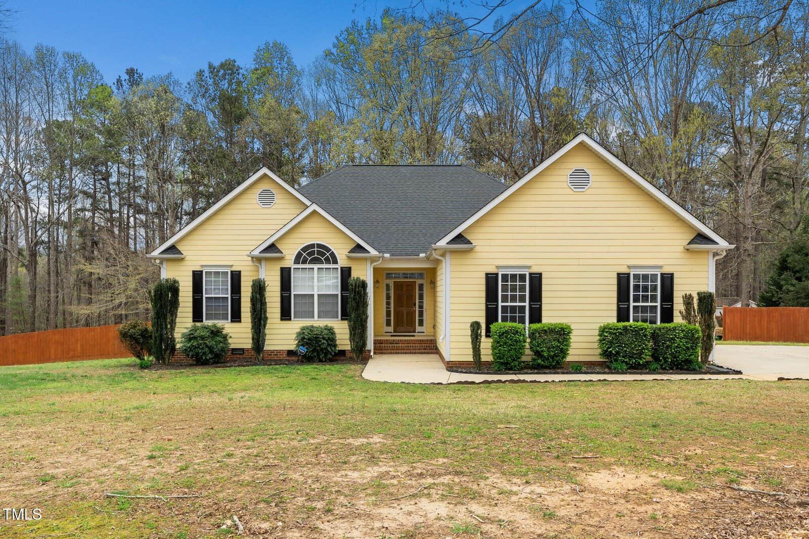 A yellow, single-story house at 1638 Crystal Lane boasts a dark roof, white trim, and symmetrical windows. The front entrance with steps is surrounded by neat shrubs. Its fenced yard with trees stands elegantly under the blue sky, creating a serene stem of suburban charm.