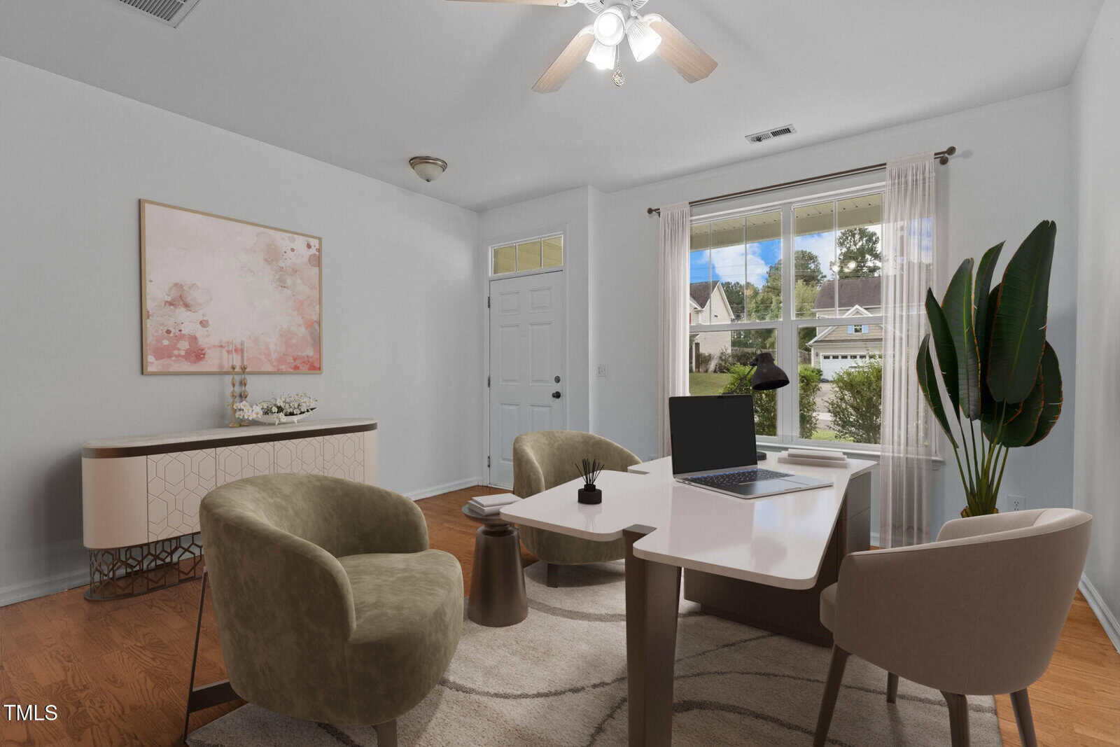 A modern office space featuring a wooden desk with a laptop and a small decorative item. Two olive green armchairs face the desk, and a beige textured chair sits behind it. A large plant and a painting are in the room, with a window showing houses outside.