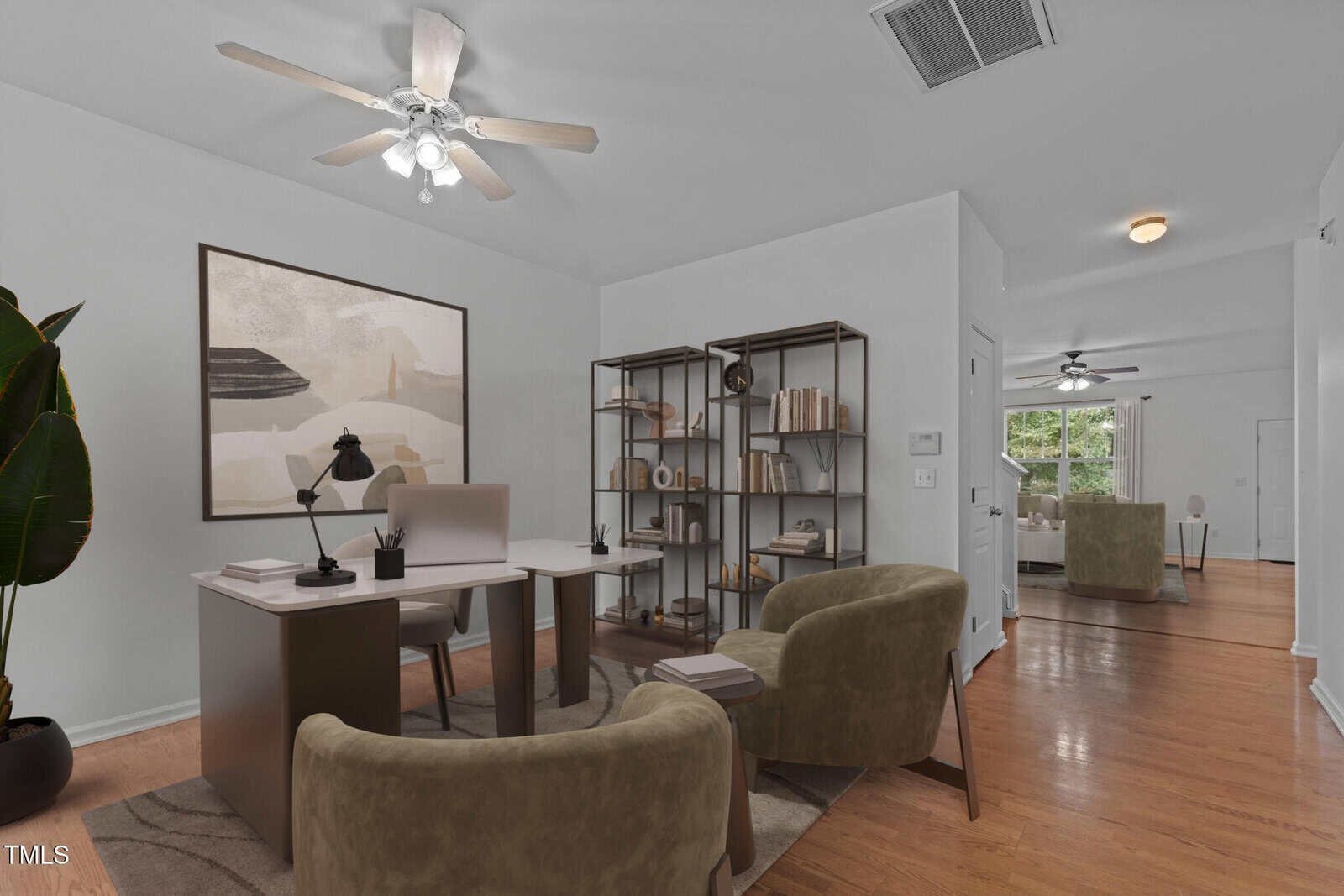 A modern, minimalist office space with a desk, a chair, and two armchairs on a rug. A tall bookshelf holds various items. A large abstract painting hangs on the wall. Hardwood floors and ceiling fans are present, with a window offering natural light.