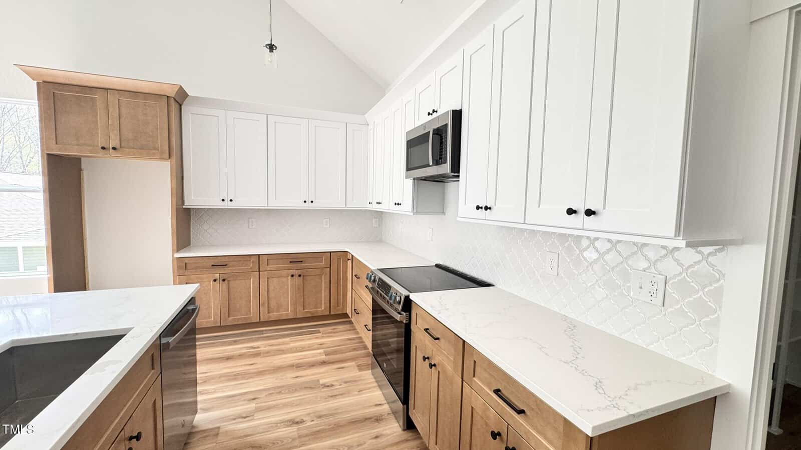 Modern kitchen with white upper cabinets, wood lower cabinets, a stainless steel stove and microwave, marble-like countertops, a white tile backsplash, and wood flooring. An island with a sink is also visible.