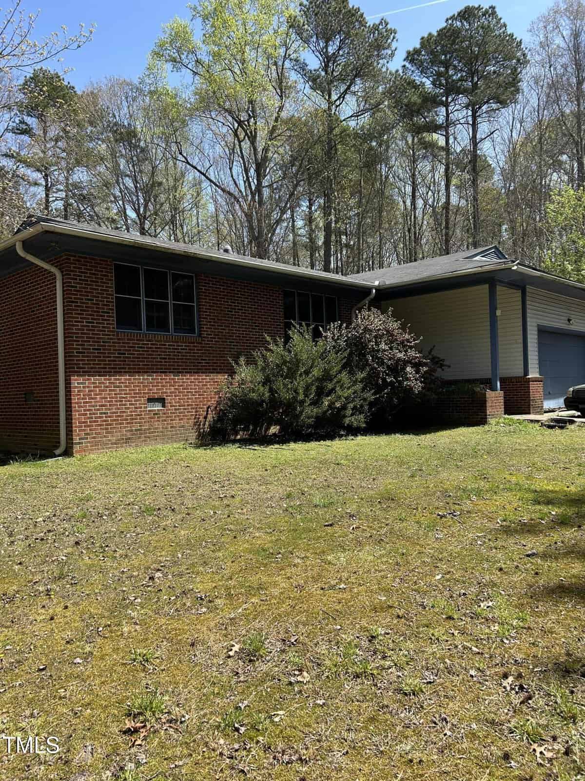A charming brick single-story house with a gabled roof and garage, nestled at 4001 W Antioch Drive, Oxford. It is surrounded by lush shrubs and trees, with a grassy lawn in the foreground and a clear blue sky providing the perfect backdrop.