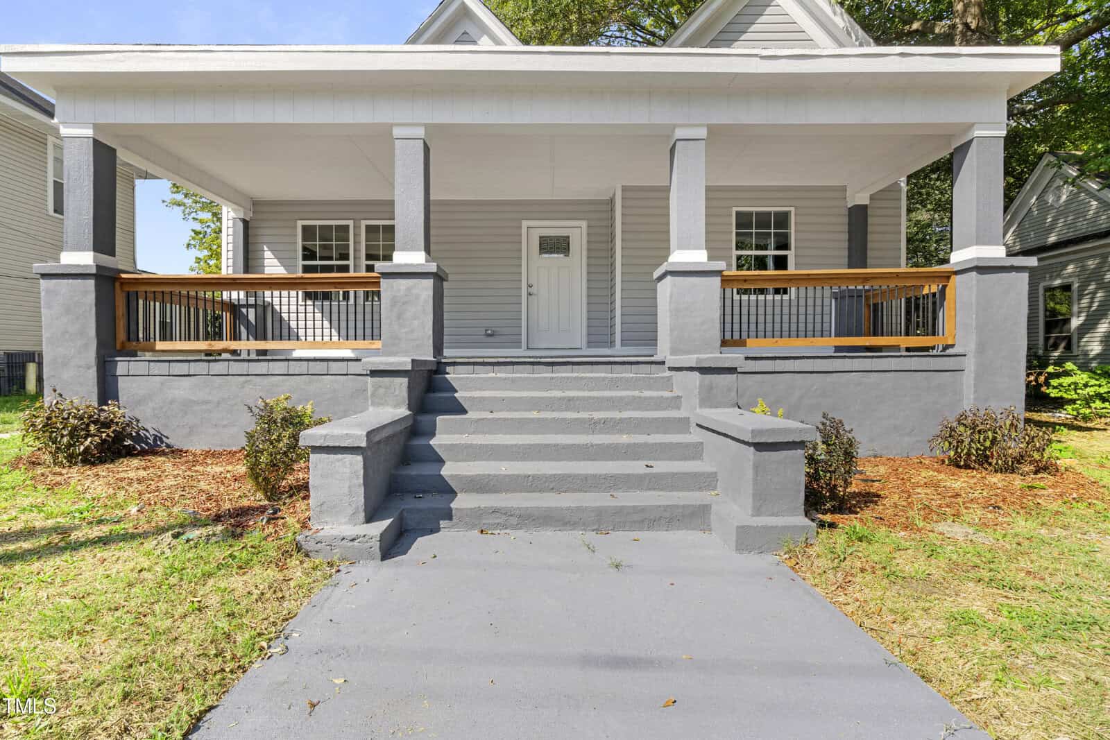 The gray house at 129 Burwell Avenue features a charming covered porch with sleek white trim. Wooden railings and concrete steps lead to the front door, while a pathway extends outwards. Small shrubs line the base of the porch, adding to its quaint appearance in Henderson.