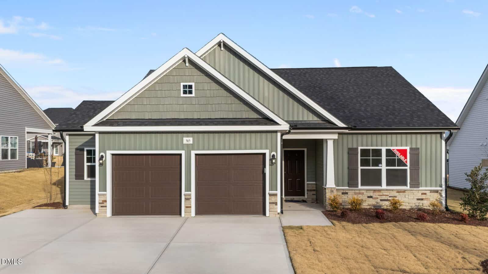 A modern, single-story house with green siding, brick accents, two brown garage doors, a covered front porch, and a red "For Sale" sign in the front window, set on a neatly landscaped yard.