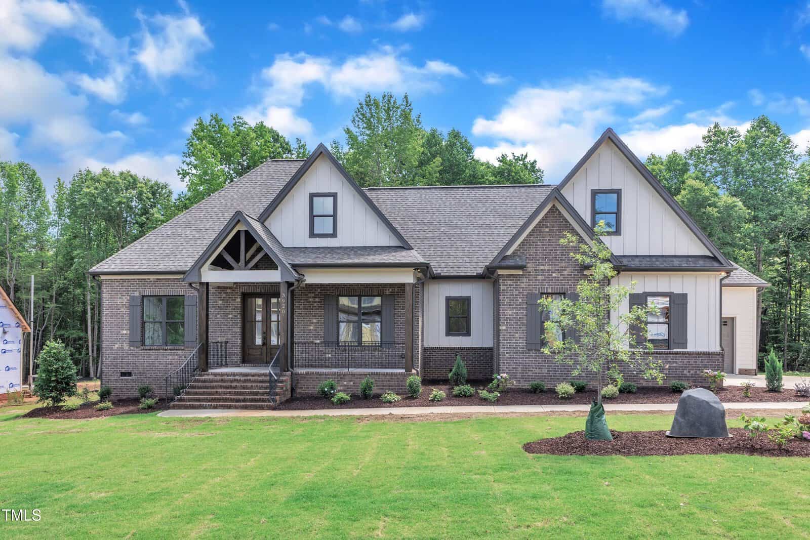 A newly built, single-story suburban house at 3920 Cedar Knolls Drive, Youngsville features dark brick and white siding exterior, gable roofs, front steps, young landscaping, and a large grassy lawn on a clear, sunny day.