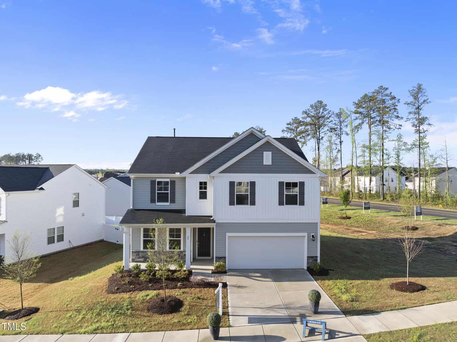 A two-story modern suburban house with white siding, gray accents, a front porch, double garage, and a well-maintained front yard. The home is situated in a residential neighborhood with trees and clear skies.