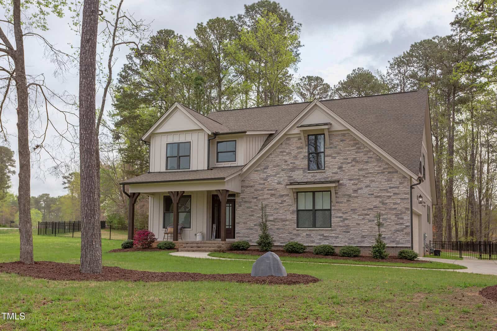 Nestled in Youngsville, the two-story house at 3881 Whisperwood Court boasts a mixed siding and stone design. Surrounded by verdant grass and trees, it features a covered front porch, multiple windows, and a trimmed lawn. A small path leads to the entrance with a rock accentuating the lush landscape.