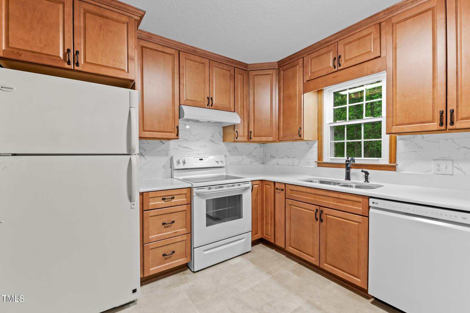 Modern kitchen with wooden cabinets, white countertops, and white appliances, including a refrigerator, oven with a range hood, and dishwasher. A window above the sink provides natural light. The backsplash features a marble pattern.