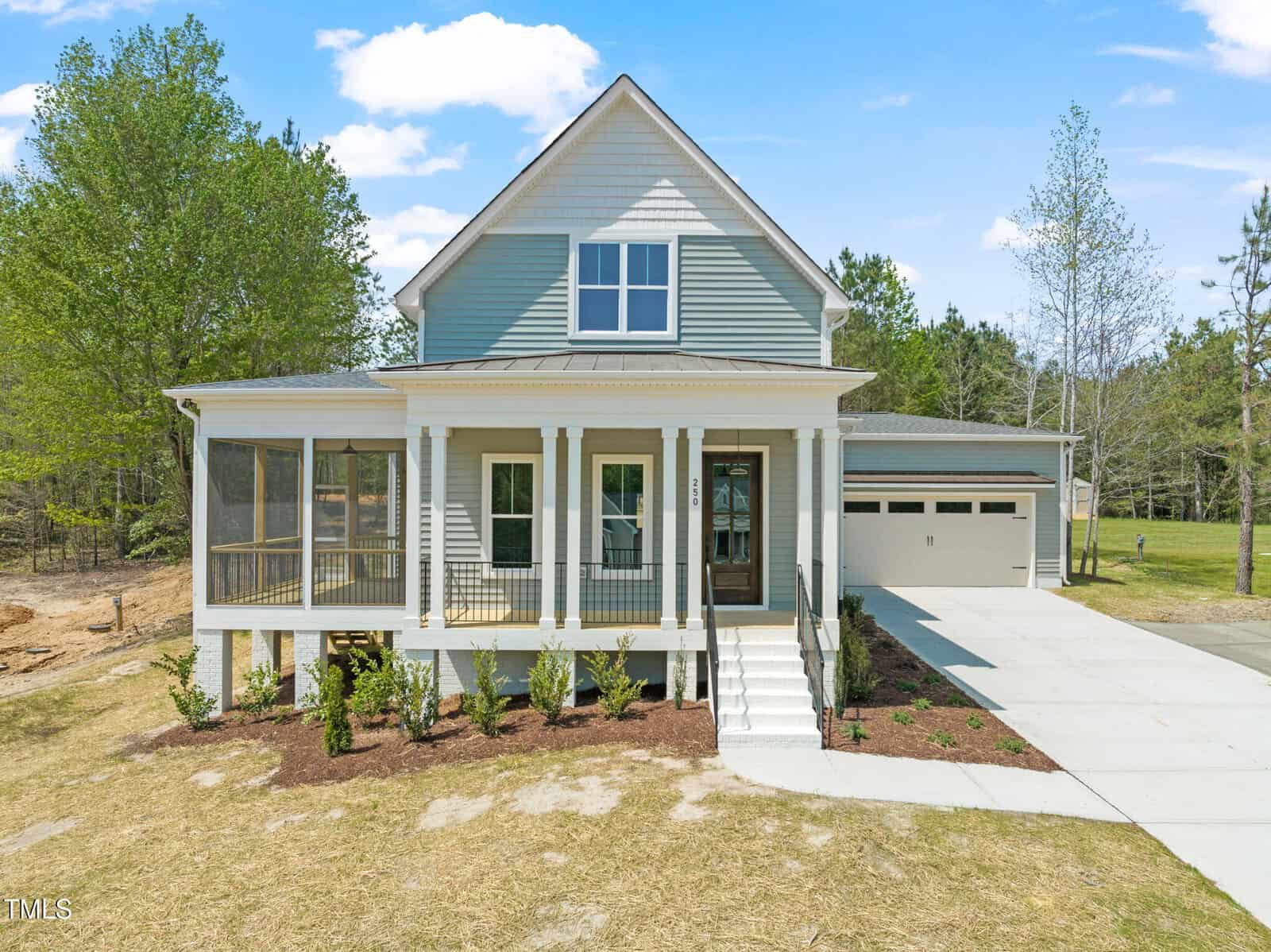 A two-story house with light blue siding, a covered front porch, screened side porch, white trim, and a two-car garage. The home sits on a grassy lot with a concrete driveway and trees in the background.