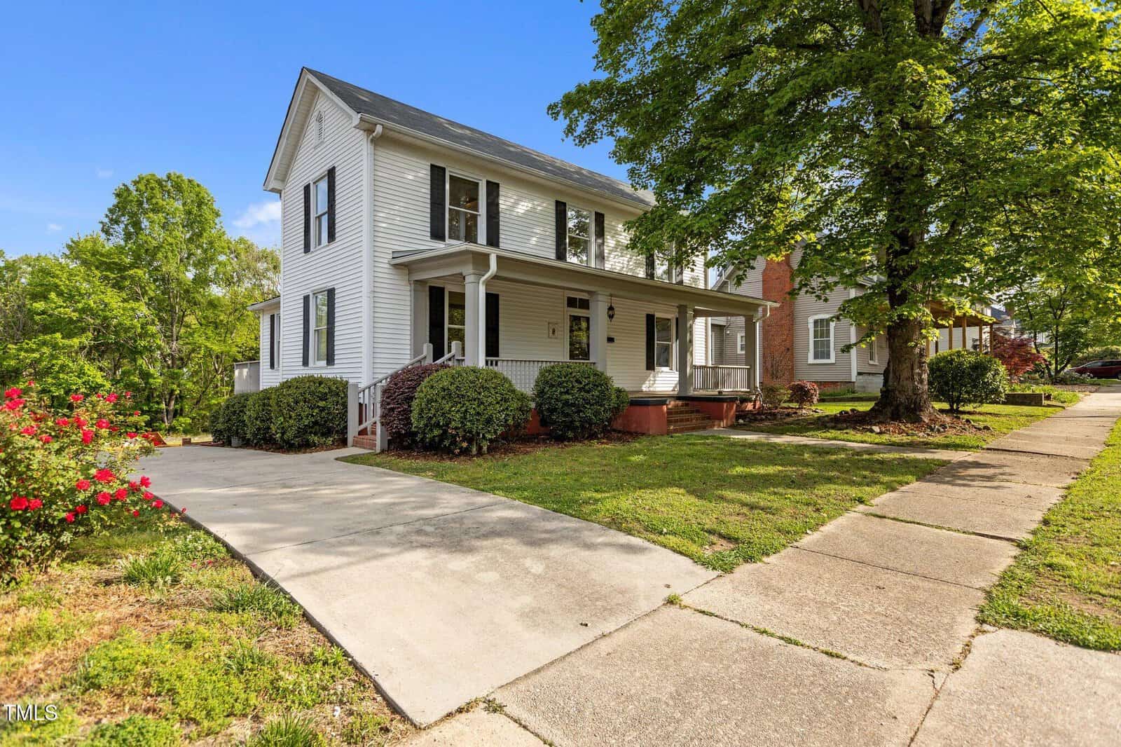 A two-story white house at 116 W Front Street in Oxford, featuring a covered front porch, black roof, and driveway, surrounded by green lawn, bushes, a tree, and a sidewalk under a clear blue sky.