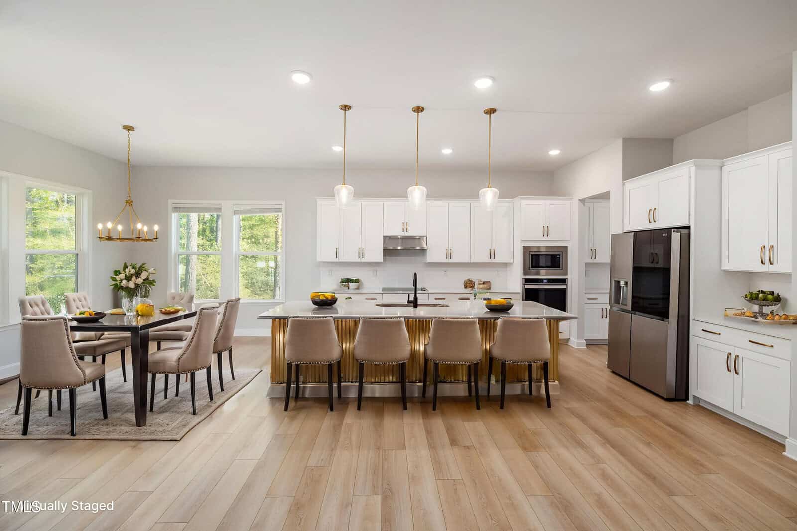 A modern kitchen with white cabinets, stainless steel appliances, a large island with six beige chairs, pendant lights above, and an adjacent dining area with a wooden table and cushioned chairs.