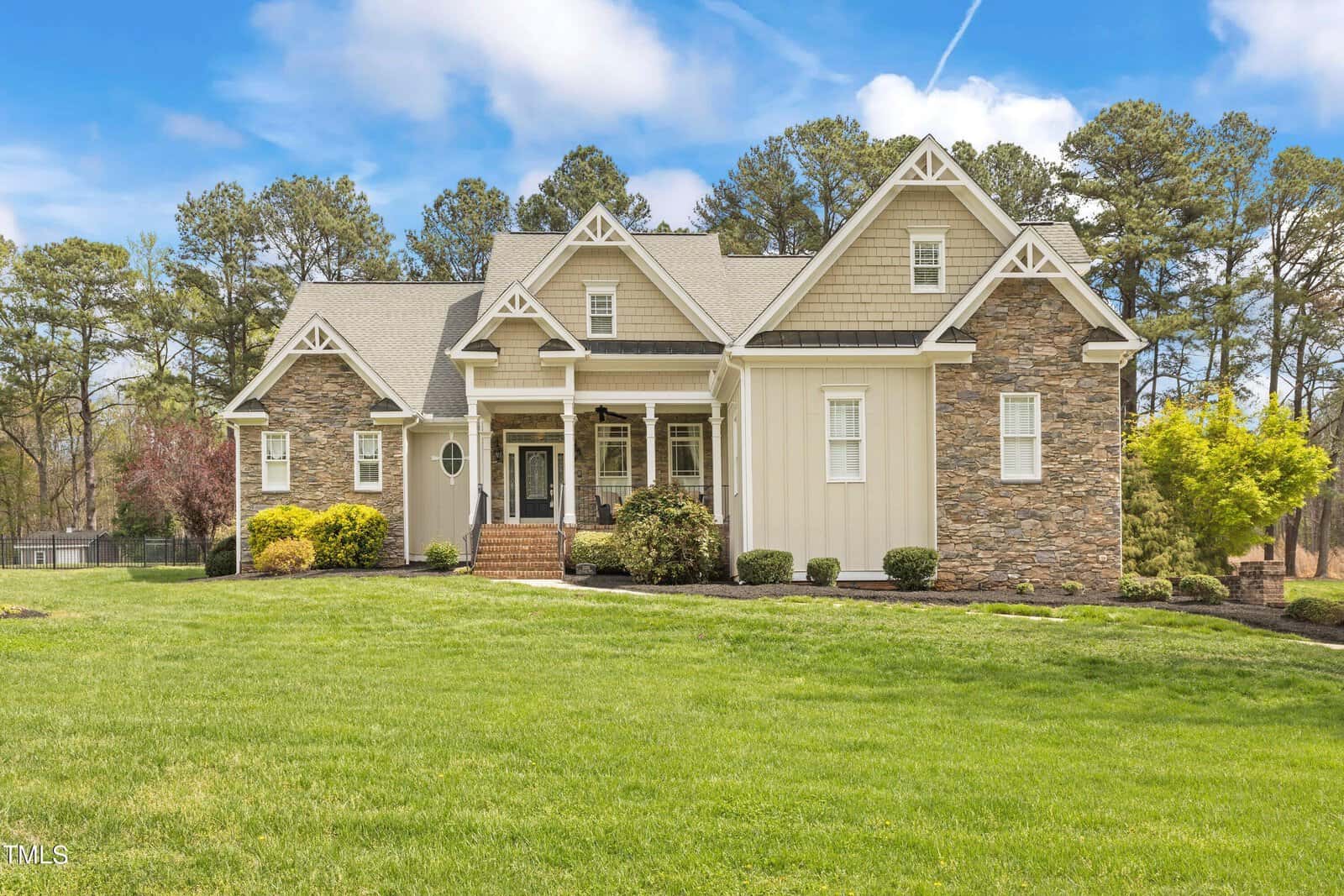 Located at 2000 Silverleaf Drive in Youngsville, this large, two-story house features a blend of stone and light-colored siding on a well-maintained lawn. The front boasts gabled roofs and a covered porch with steps leading up. Trees and a clear sky enhance the scenic backdrop.