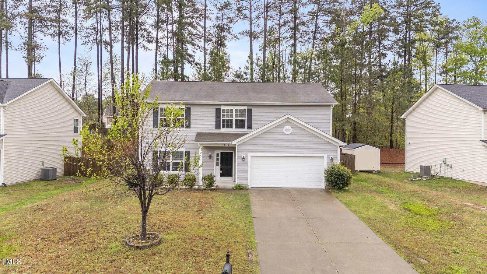 A two-story gray house with white trim on 2214 Bayswater Drive features a charming front porch, double garage, and a small tree in the yard. Nestled in the Creedmoor area, it's flanked by similar homes with tall trees providing a serene backdrop.