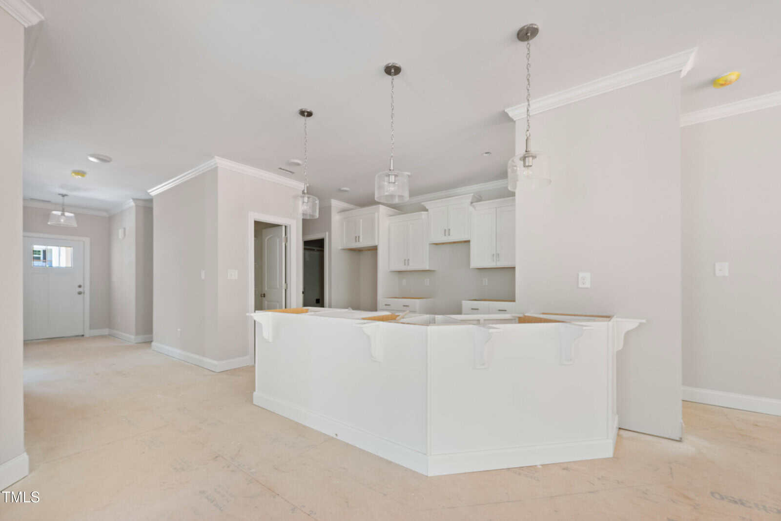A newly constructed kitchen with white cabinets and a large white island. The room has light-colored walls, three pendant lights above the island, and unfinished flooring. There are no appliances or furniture present.