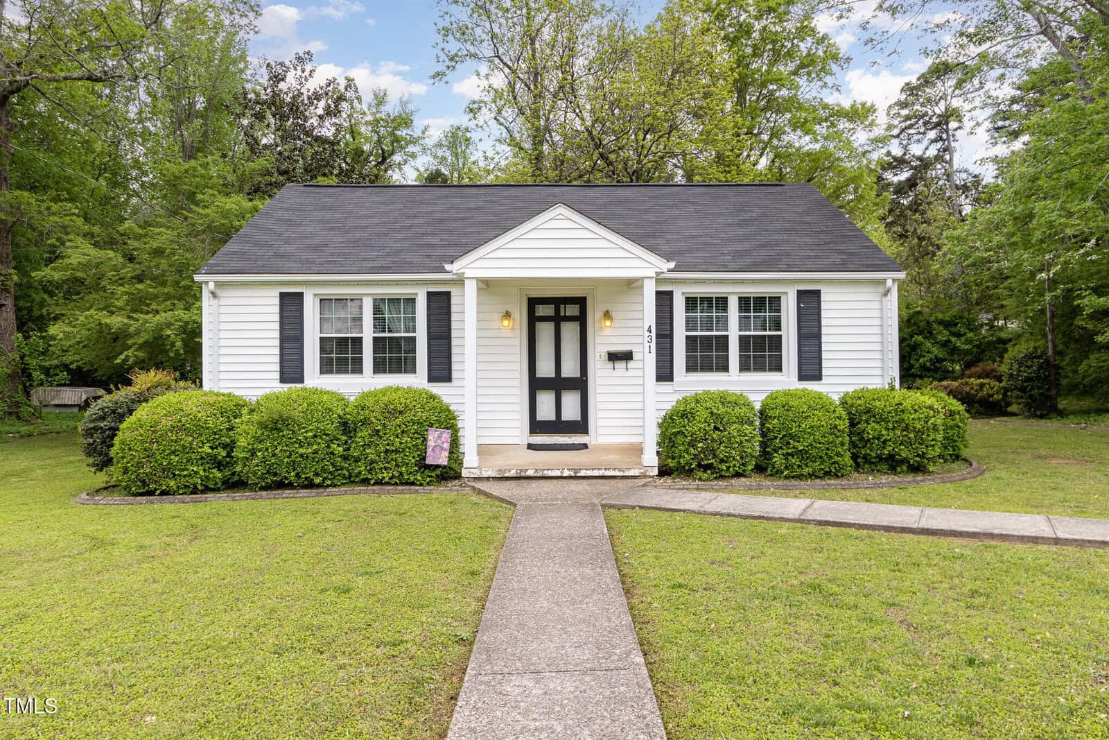 A small single-story white house with a dark roof, black shutters, and a covered front porch sits at 431 Waddill Street in Henderson. Trimmed bushes and a green lawn frame the concrete walkway leading to the front door, with trees in the background.