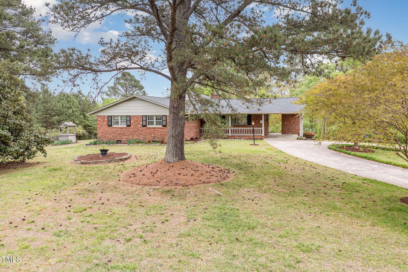 A single-story brick house at 1750 Spring Valley Lake Road, Henderson, features a front porch, grassy yard with trees, and a curved driveway. Shrubs and landscaping enhance the home's welcoming entrance.