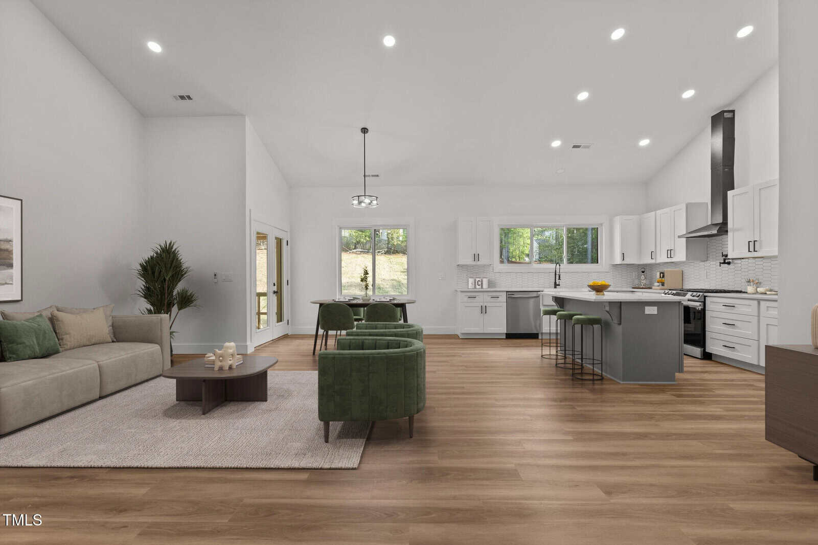 Spacious open-concept living area with light wood floors, modern kitchen with island, green chairs, beige sofa, large windows, and recessed lighting. Dining area and sliding glass door lead to the outside.