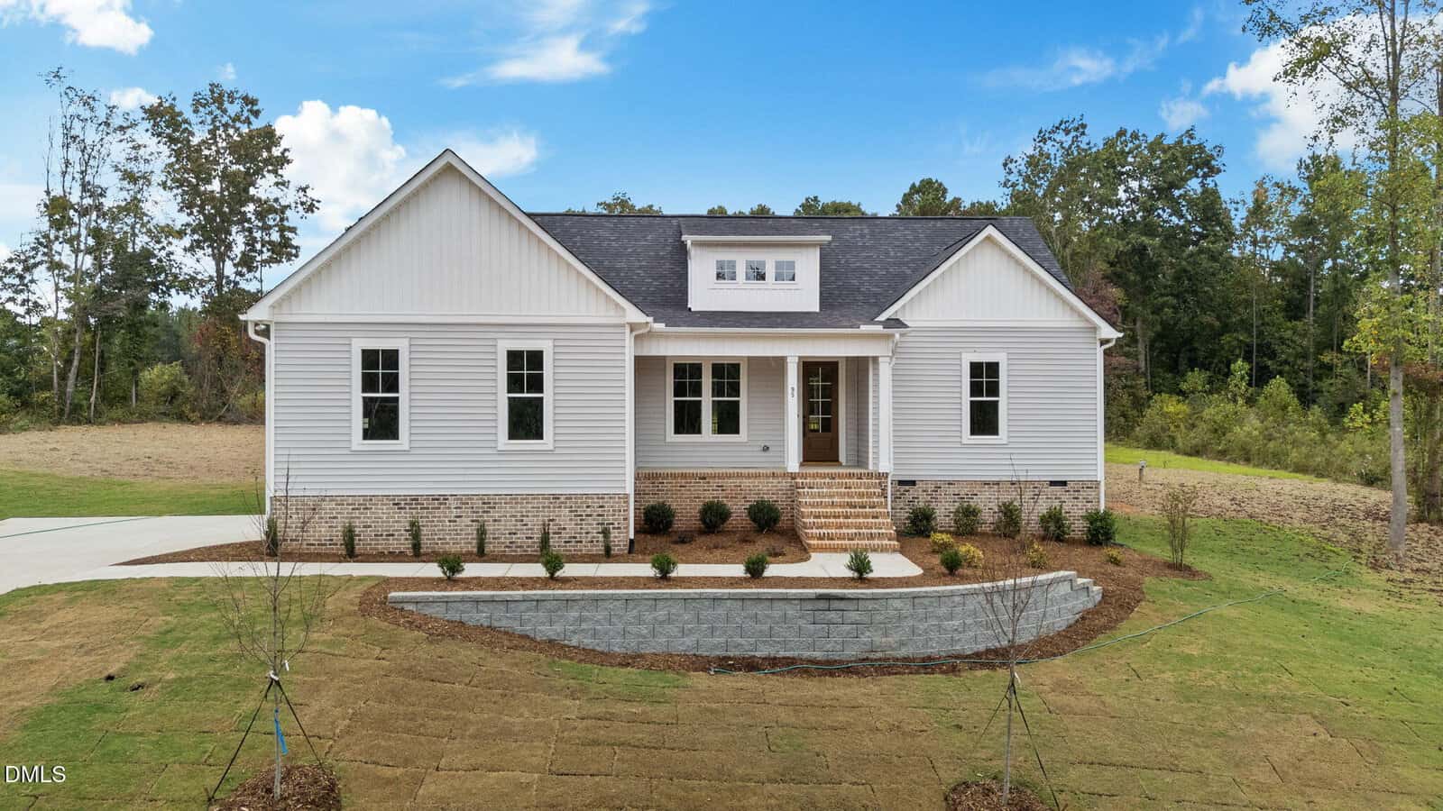 A single-story white house with a dark roof, brick foundation, and front porch sits at 95 Autumnwood Lane, Zebulon. The yard is newly landscaped with shrubs and fresh sod, surrounded by trees under a blue sky with scattered clouds.