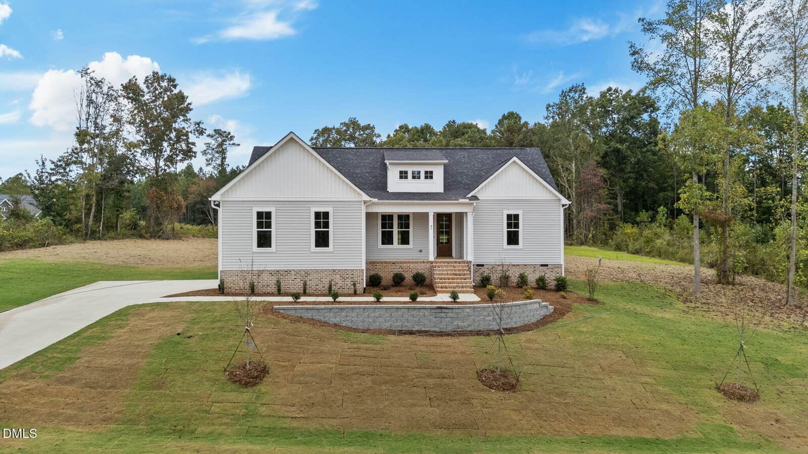 Single-story white house with a dark roof, front porch, and brick steps. The house has a long driveway on the left and freshly laid sod in the front yard, surrounded by trees and blue sky in the background.