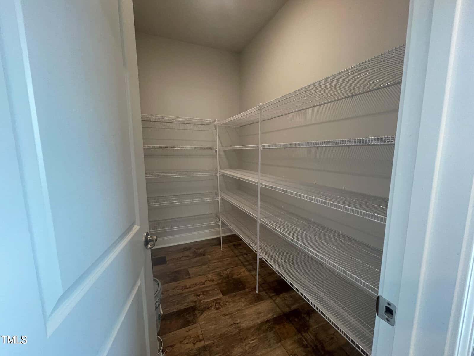 A walk-in pantry with white wire shelving on both sides and back wall, empty shelves, a tiled floor, and white walls, viewed from the open doorway.