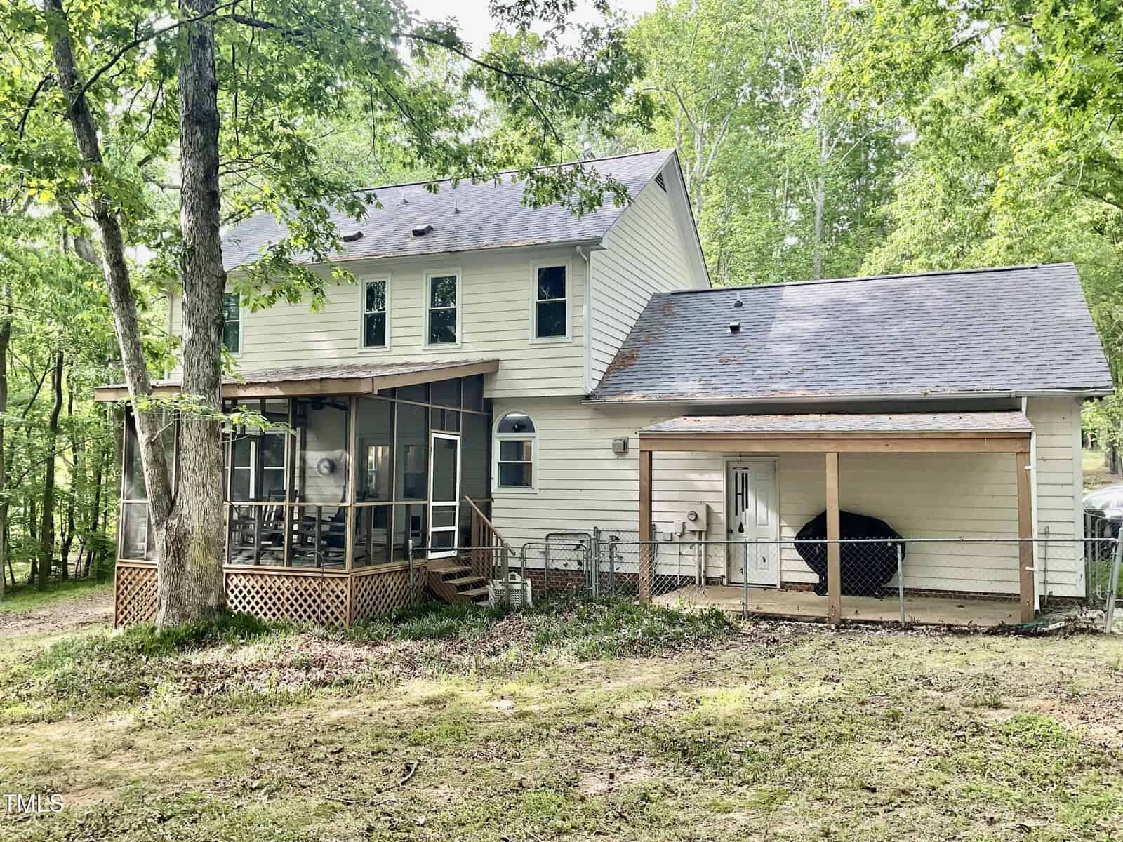 A two-story beige house with a screened porch, attached garage, and fenced area in the backyard, surrounded by trees and greenery on a slightly sloped lot.