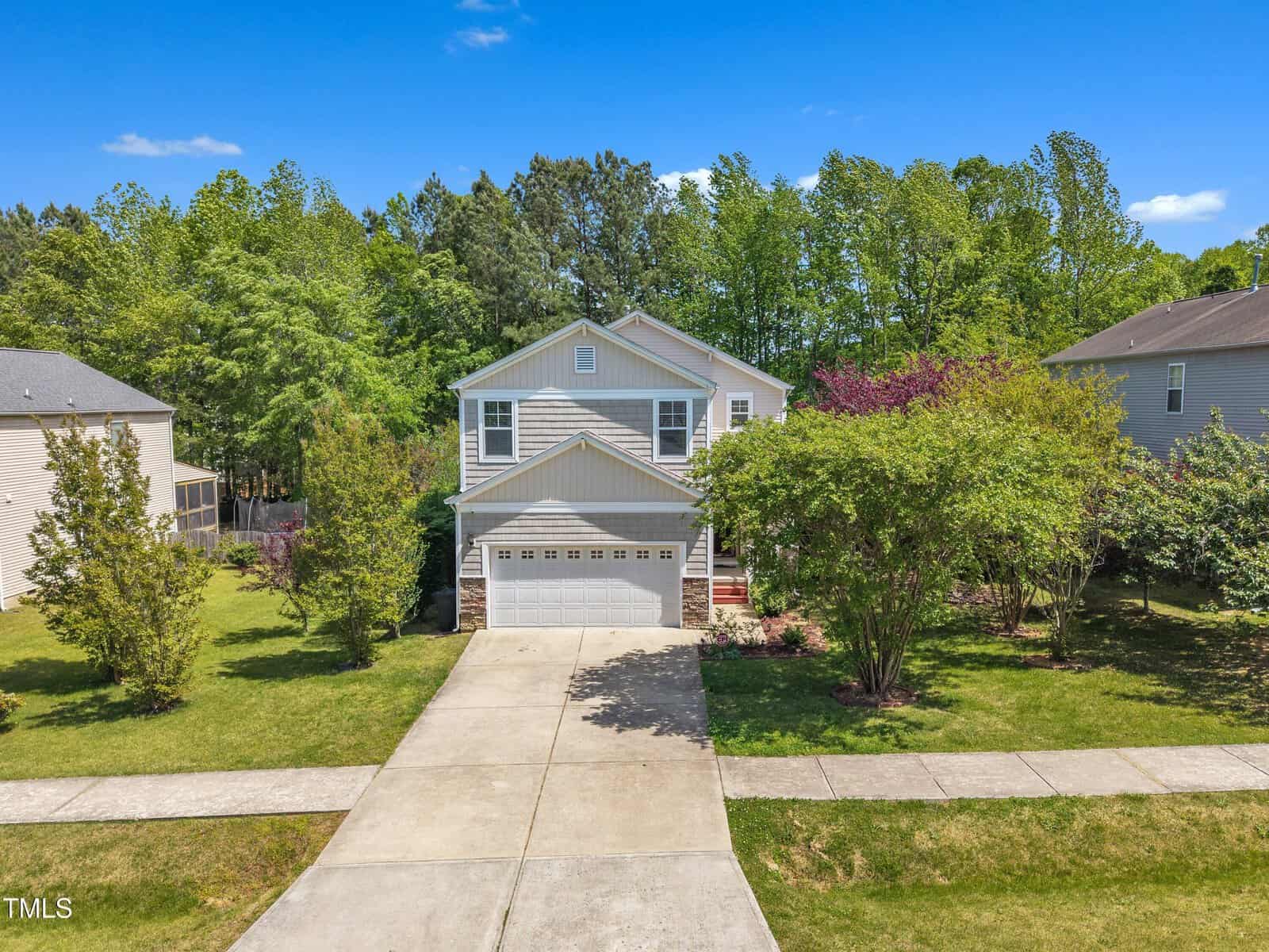 A two-story suburban house at 1198 Shining Water Lane, Creedmoor, with a two-car garage, gray siding, and white trim, surrounded by green lawns and trees. The driveway leads to the street with neighboring homes on either side.
