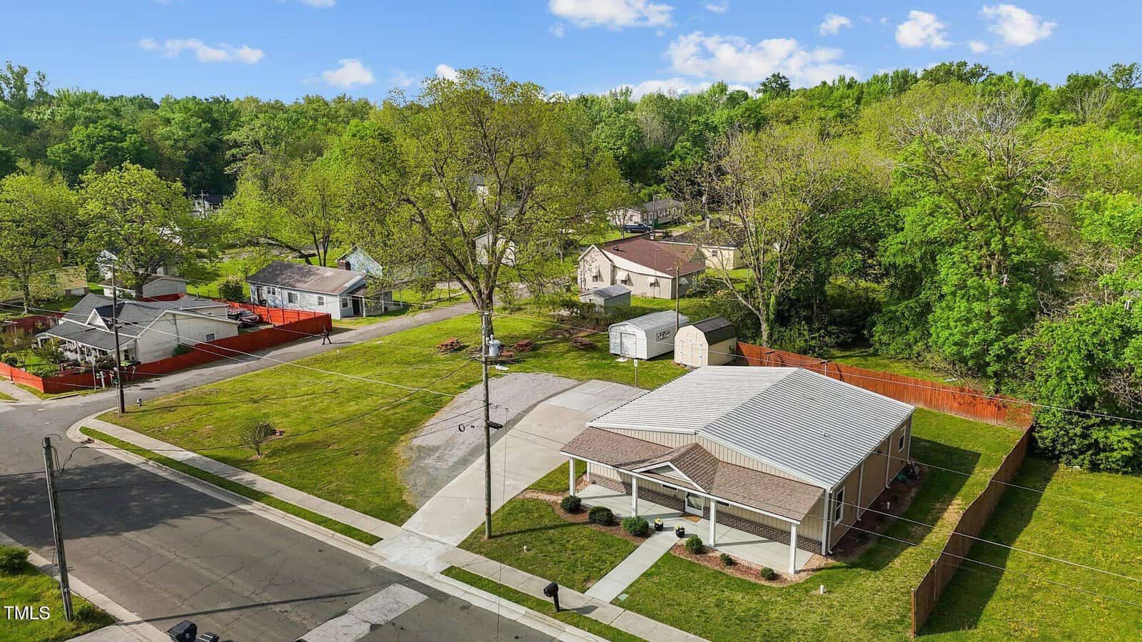 A single-story house with a covered porch sits on a corner lot at 212 Orange Street, Oxford. The large, neatly mowed lawn is surrounded by nearby houses and trees, while two storage sheds are visible in the backyard.