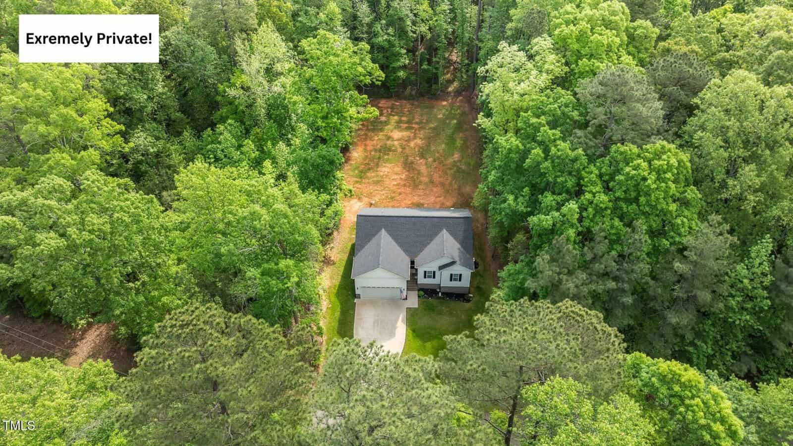 A house with a gray roof is surrounded by dense green trees, set at the end of a long driveway; a caption in the top left reads "Extremely Private!.