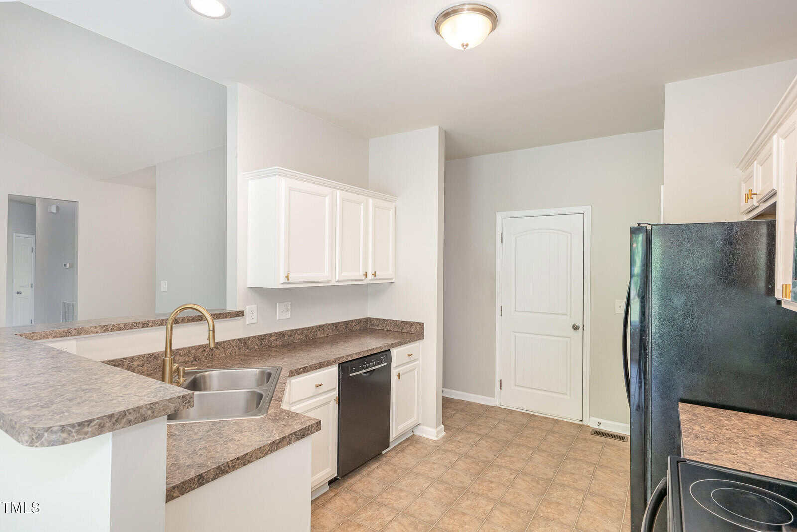 Modern kitchen with white cabinets, granite countertops, stainless steel sink, black dishwasher, black refrigerator, and tile flooring. There is a white door and neutral wall paint. Lighting is from ceiling fixtures.