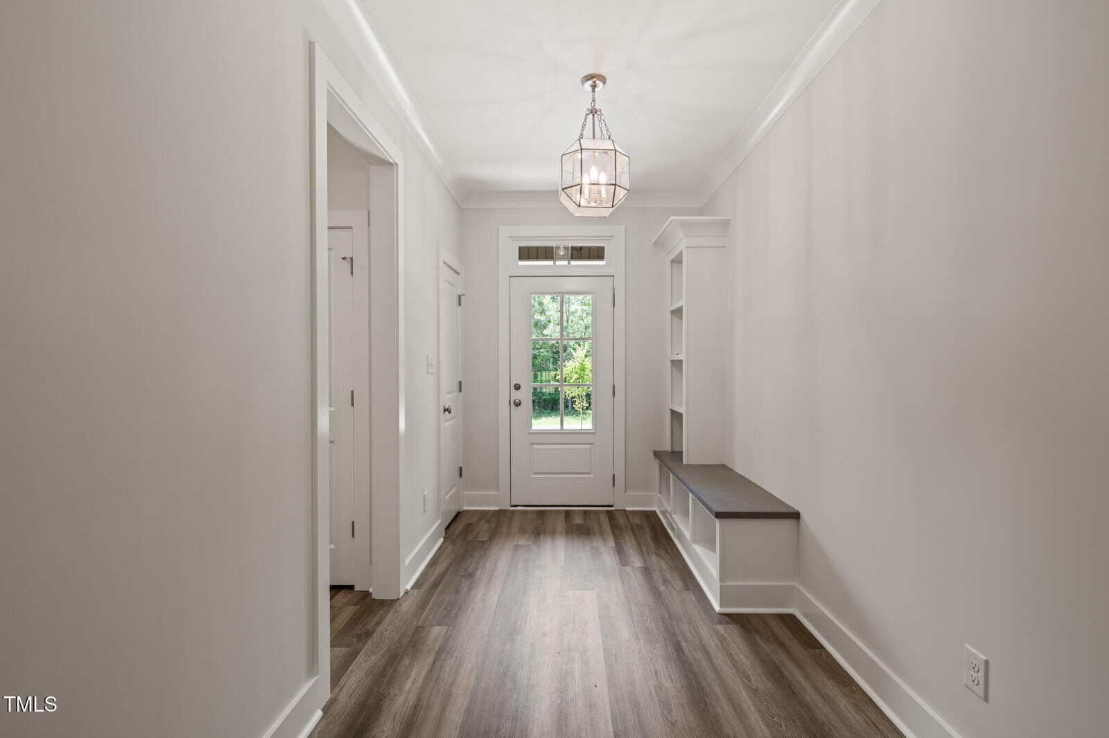 A bright entryway with light gray walls, wood flooring, a glass door with side windows, a bench with shelves on the right, and a geometric pendant light hanging from the ceiling.
