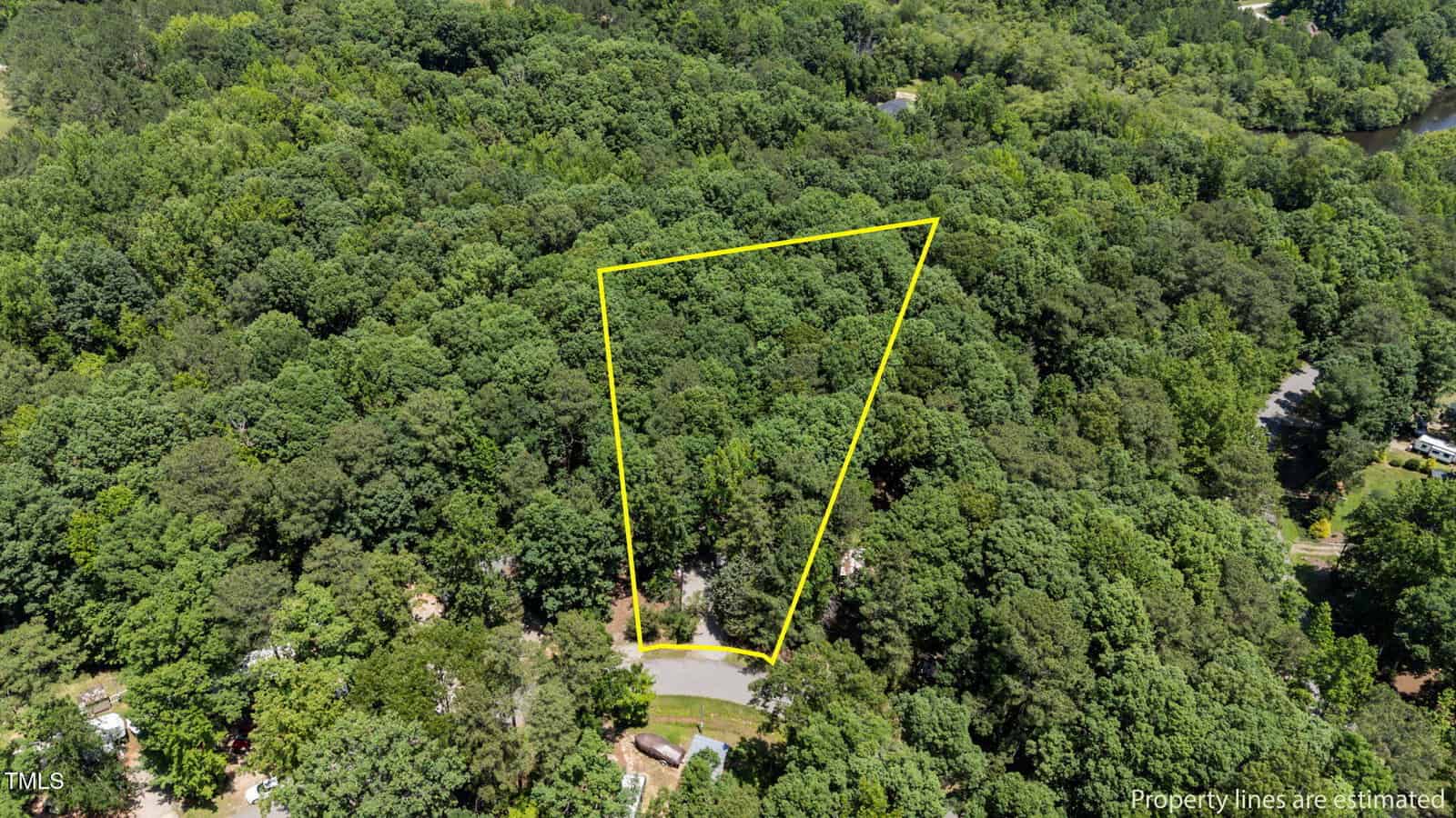 Aerial view of a densely wooded lot bordered by a yellow outline, showing estimated property lines on a cul-de-sac surrounded by lush green trees and nearby houses.