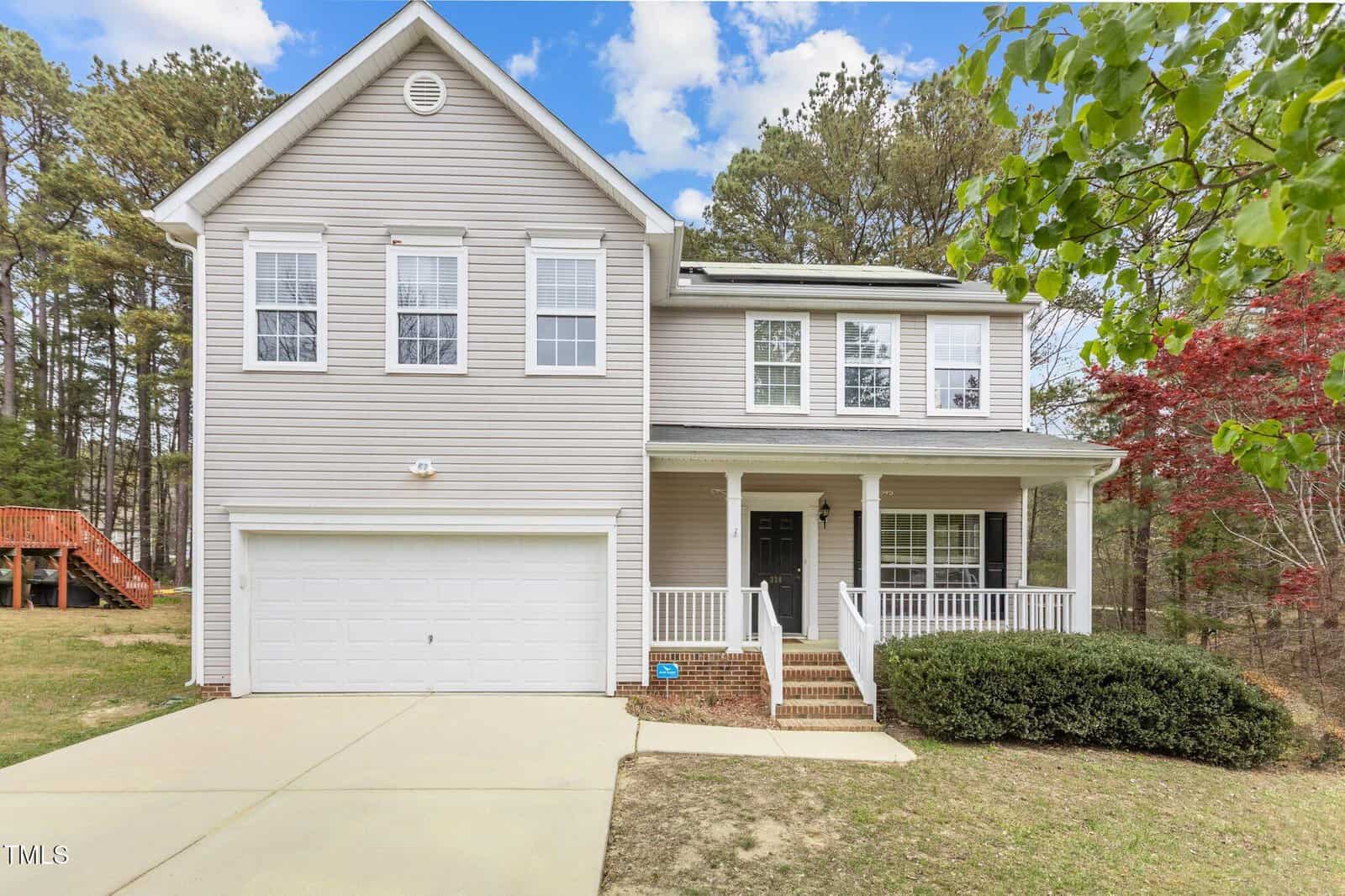 A two-story beige house with white trim at 338 Howland Court, Creedmoor. Features a front porch, attached two-car garage, and a driveway leading to the entrance. Trees and a lawn surround this inviting property.