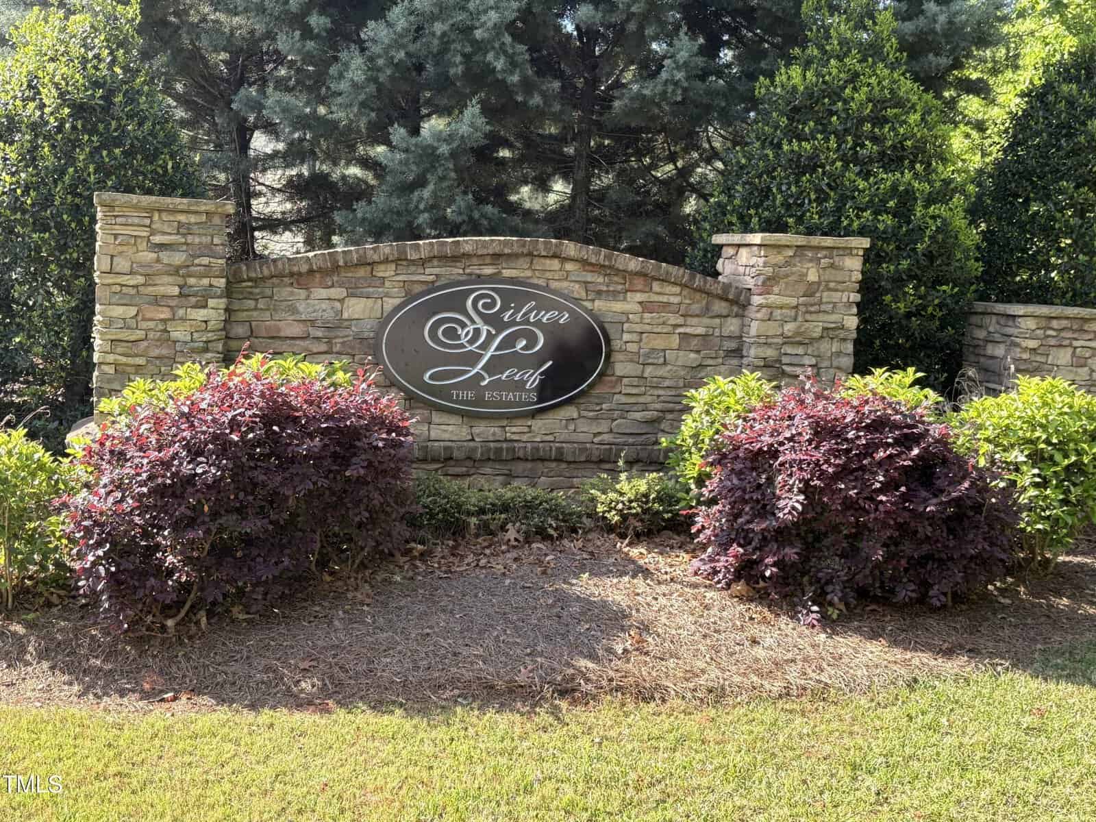 A stone wall with a black oval sign reading "Silver Leaf The Estates" in white script stands at 1123 Dovefield Lane, Youngsville, surrounded by neatly trimmed bushes and tall green trees in the background.