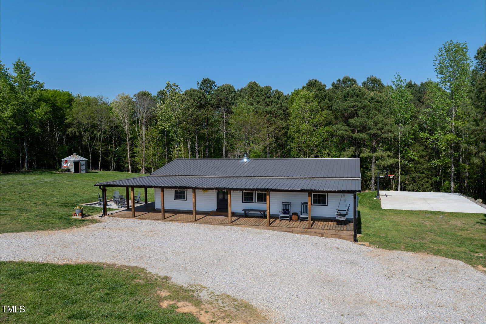 A single-story house at 435 Salt And Light Lane, Henderson, features a metal roof and covered front porch on a gravel driveway, surrounded by green grass and trees. A small shed and concrete pad are visible in the background.